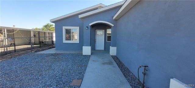 view of exterior entry featuring fence and stucco siding