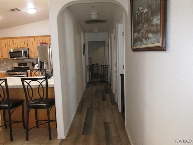 corridor featuring arched walkways, visible vents, and baseboards