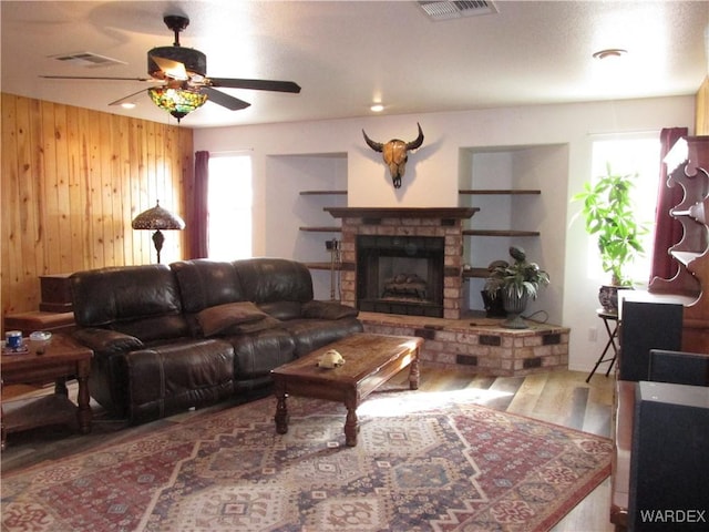 living room with visible vents, wood walls, a fireplace, and wood finished floors