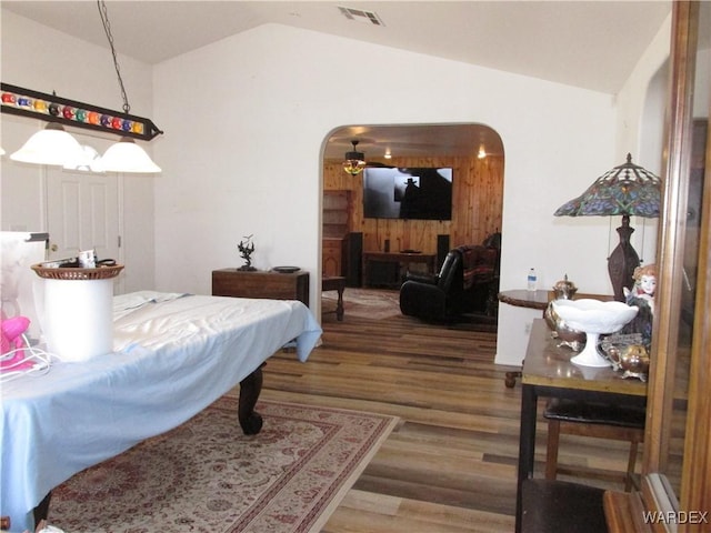 bedroom with arched walkways, vaulted ceiling, wood finished floors, and visible vents