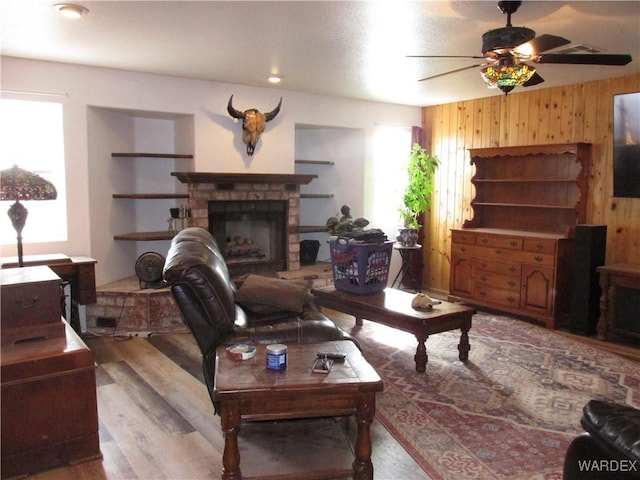 living room featuring ceiling fan, a fireplace with raised hearth, wood walls, and wood finished floors