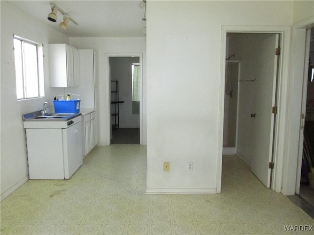 kitchen featuring baseboards, rail lighting, light countertops, white cabinetry, and a sink