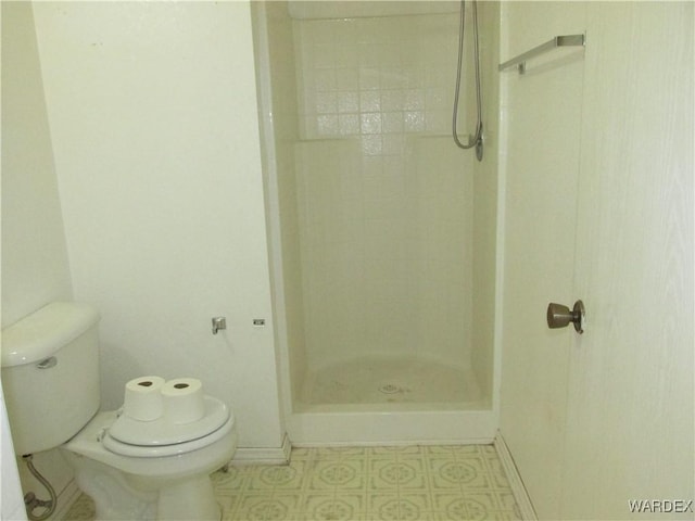 bathroom with toilet, a stall shower, and baseboards