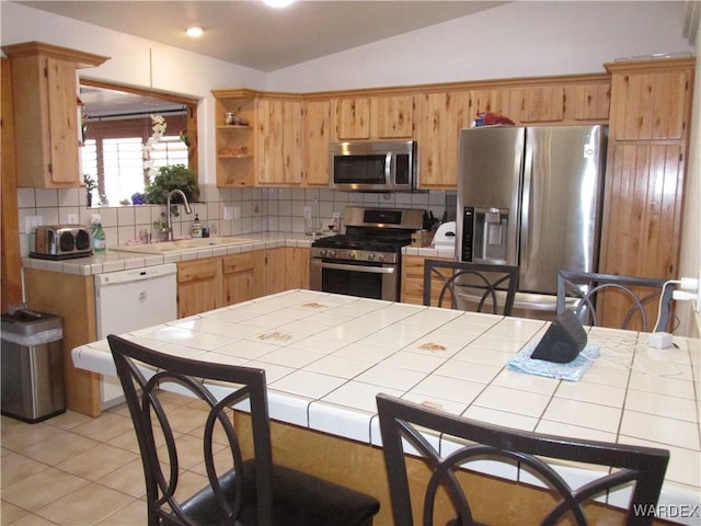 kitchen with tile countertops, stainless steel appliances, a sink, vaulted ceiling, and decorative backsplash