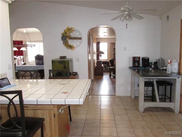 interior space with tile countertops, ceiling fan, light tile patterned flooring, and arched walkways