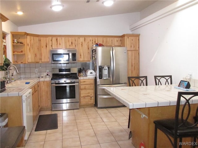 kitchen with stainless steel appliances, tile counters, a sink, and decorative backsplash