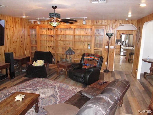 living area featuring arched walkways, wood walls, wood finished floors, and visible vents