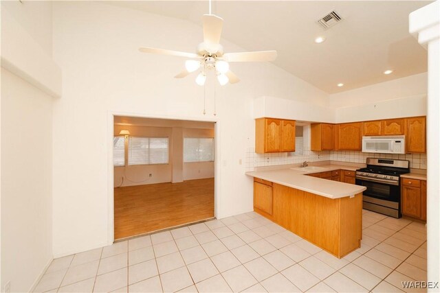 kitchen featuring stainless steel gas range oven, white microwave, a peninsula, visible vents, and light countertops