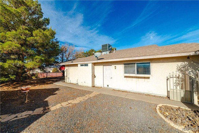 rear view of house with roof with shingles, fence, cooling unit, and stucco siding