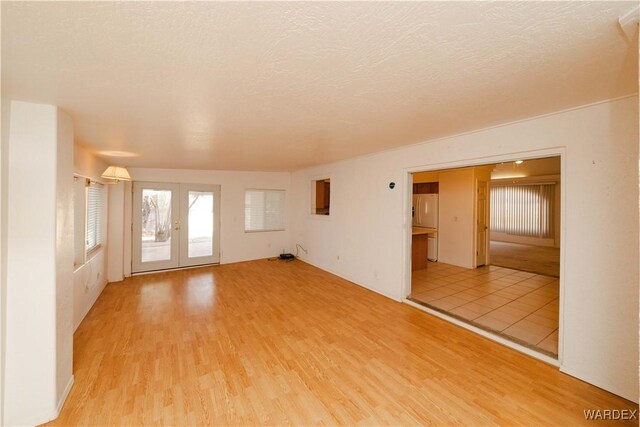 unfurnished room with light wood finished floors, french doors, and a textured ceiling