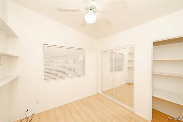 unfurnished bedroom with lofted ceiling, wood finished floors, a ceiling fan, and multiple closets