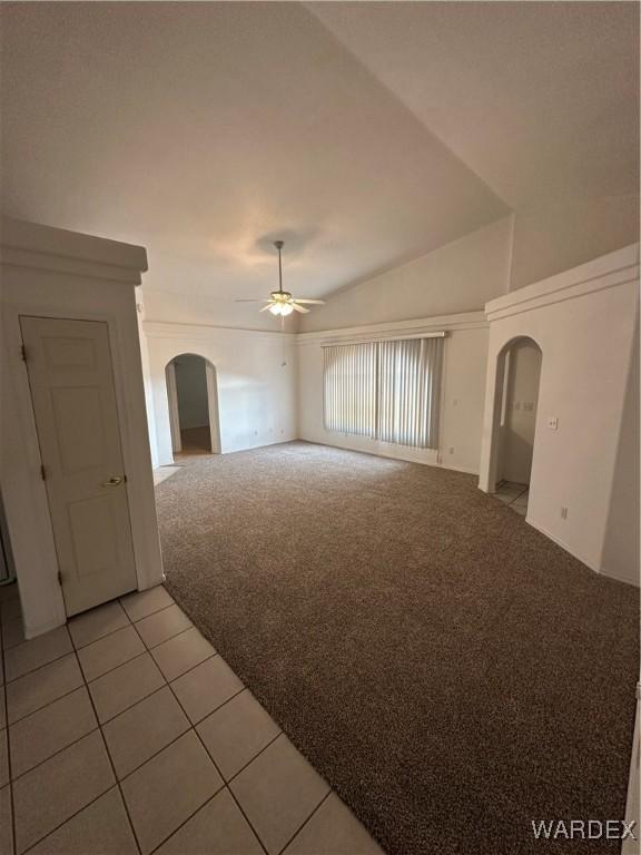 unfurnished living room featuring light carpet, light tile patterned floors, arched walkways, a ceiling fan, and lofted ceiling