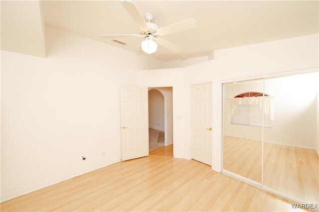 unfurnished bedroom with arched walkways, visible vents, a ceiling fan, a closet, and light wood-type flooring