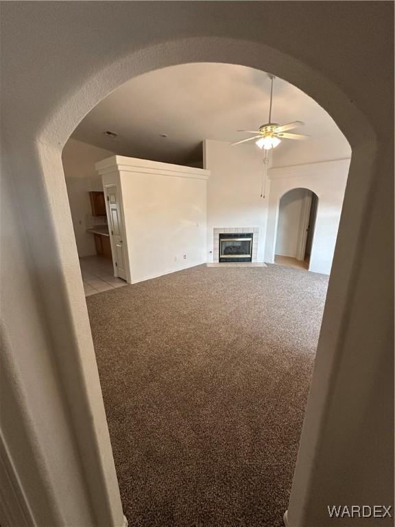 unfurnished living room with light carpet, arched walkways, a ceiling fan, and a tile fireplace