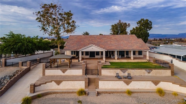 view of front of home with a mountain view, fence, a tiled roof, a gazebo, and a patio area