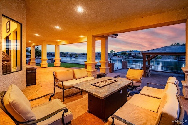 patio terrace at dusk with an outdoor living space with a fire pit, a water view, fence, and a gazebo