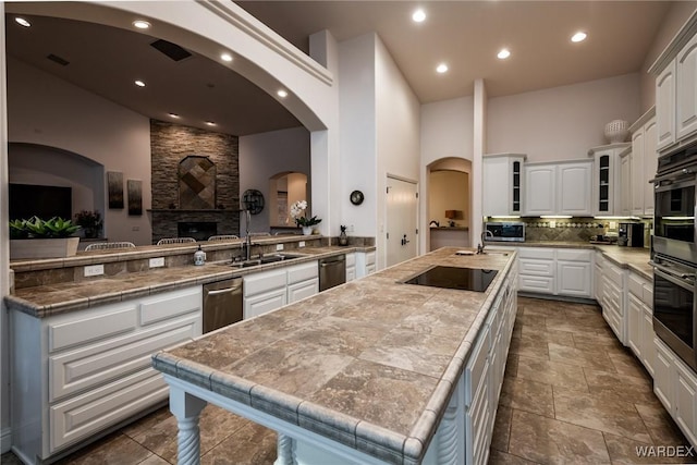 kitchen with white cabinets, tile countertops, glass insert cabinets, appliances with stainless steel finishes, and a kitchen island with sink