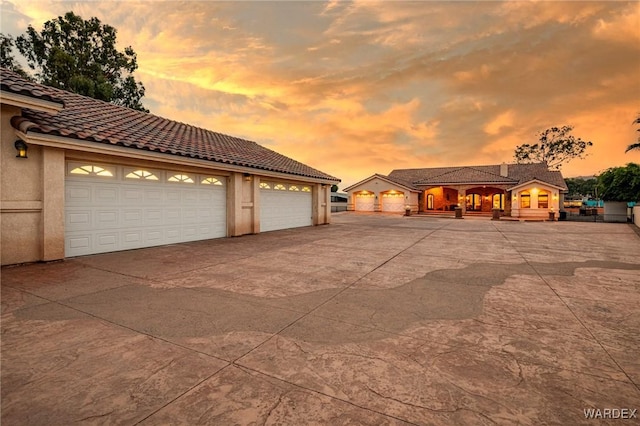 view of front of home with a garage, concrete driveway, a tile roof, and stucco siding