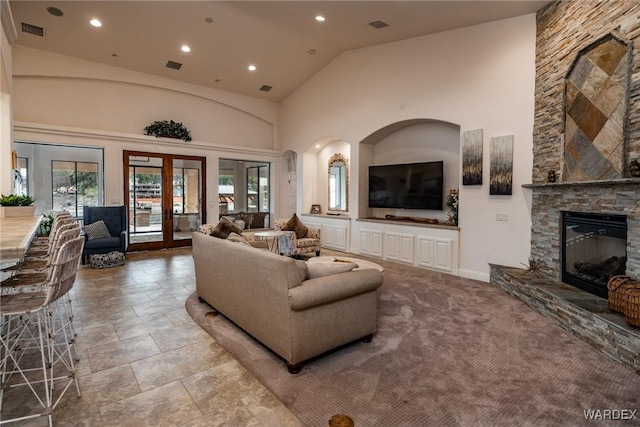 living room featuring high vaulted ceiling, a stone fireplace, plenty of natural light, and french doors