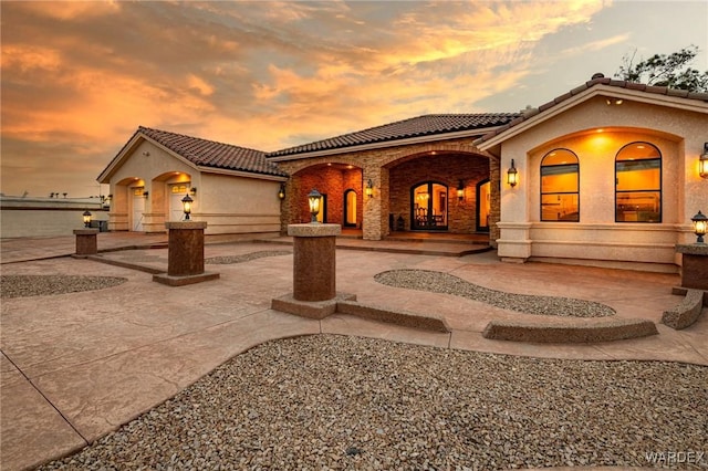 back of house featuring driveway, a patio area, a tiled roof, and stucco siding