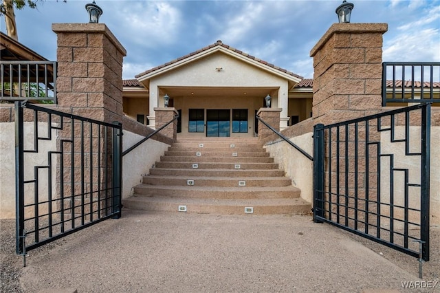 exterior space featuring a tile roof, a gate, fence, and stucco siding