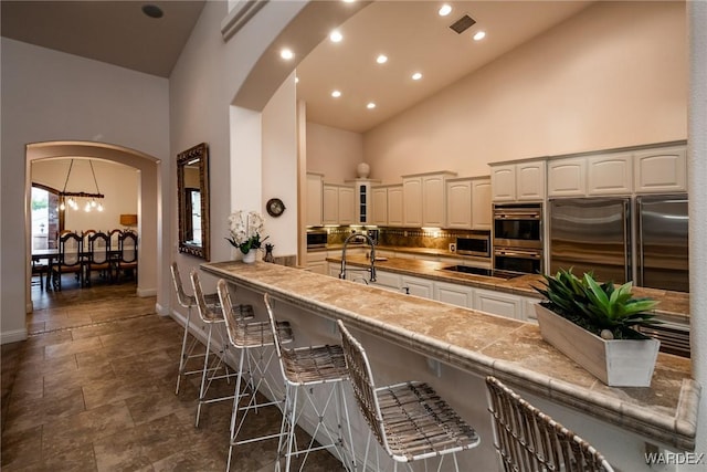 kitchen with arched walkways, stainless steel appliances, glass insert cabinets, white cabinetry, and high vaulted ceiling