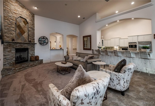 living room featuring arched walkways, high vaulted ceiling, a stone fireplace, recessed lighting, and baseboards