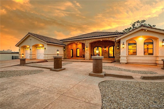 back of property with a tiled roof, curved driveway, stone siding, and stucco siding