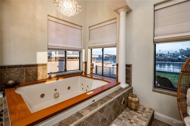 full bathroom featuring a water view, decorative columns, a whirlpool tub, and an inviting chandelier