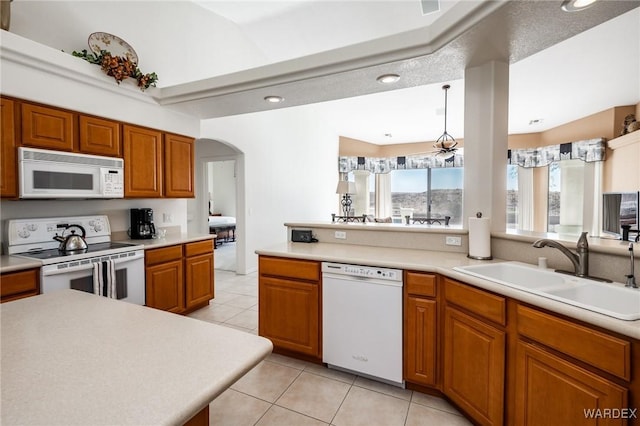 kitchen featuring arched walkways, white appliances, a sink, light countertops, and brown cabinetry