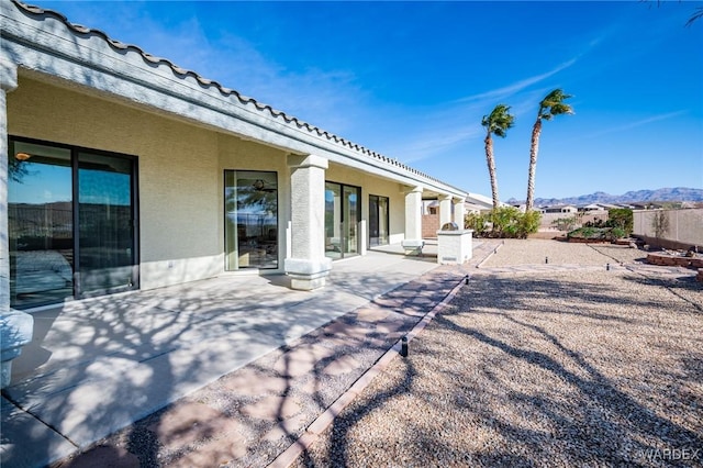 rear view of house featuring a patio, a mountain view, fence, a tiled roof, and stucco siding