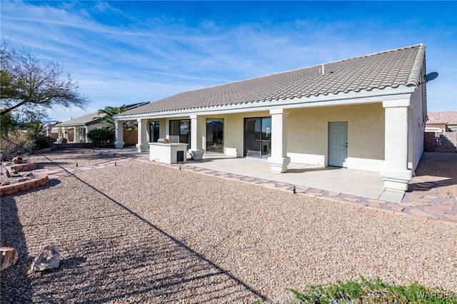 rear view of house with a patio area, a tile roof, and stucco siding