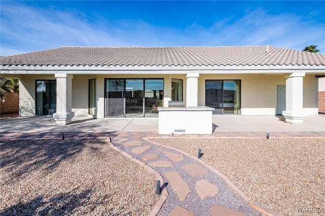 back of house featuring a tile roof, a patio, and stucco siding