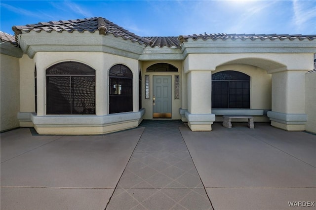 entrance to property featuring a patio area, a tile roof, and stucco siding