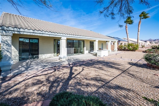 rear view of house with a patio, a tiled roof, and stucco siding