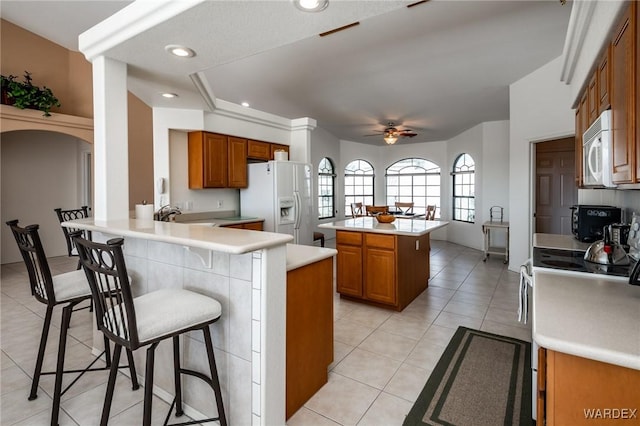 kitchen featuring brown cabinetry, white appliances, light countertops, and a peninsula