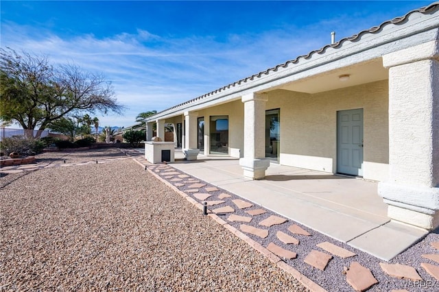 rear view of house featuring a patio, a tiled roof, and stucco siding