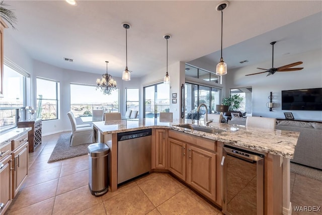 kitchen with light stone counters, hanging light fixtures, stainless steel dishwasher, open floor plan, and a sink