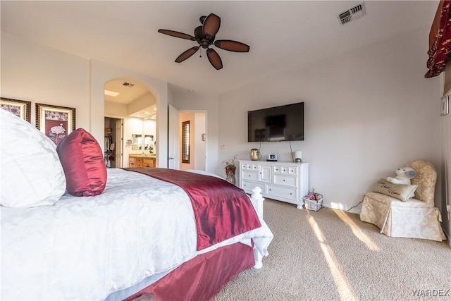 carpeted bedroom with a ceiling fan, arched walkways, visible vents, and ensuite bathroom