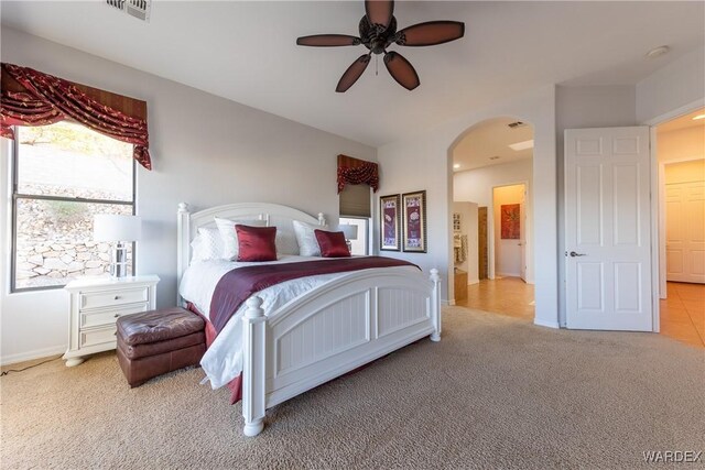 carpeted bedroom with arched walkways, visible vents, ceiling fan, and baseboards