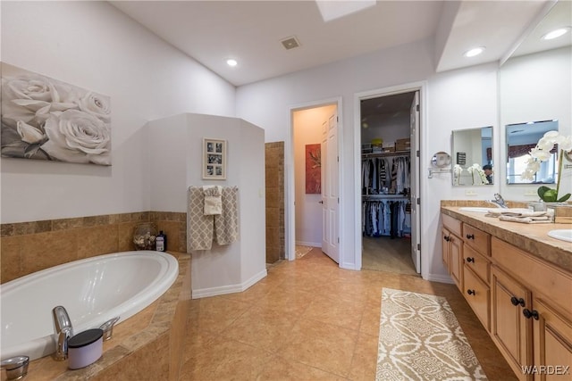 full bath with double vanity, visible vents, a garden tub, a walk in closet, and a sink