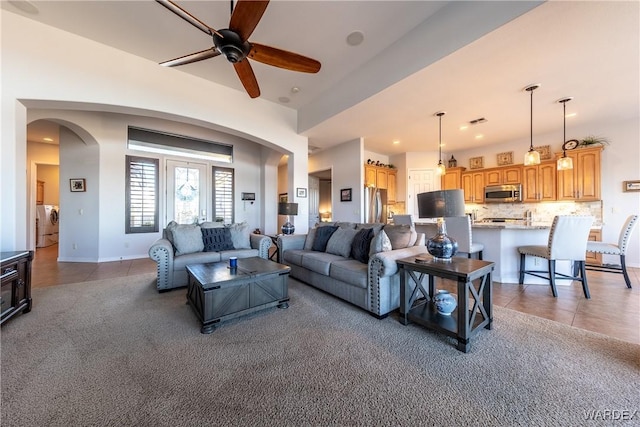 living area with arched walkways, ceiling fan, light tile patterned flooring, light carpet, and visible vents