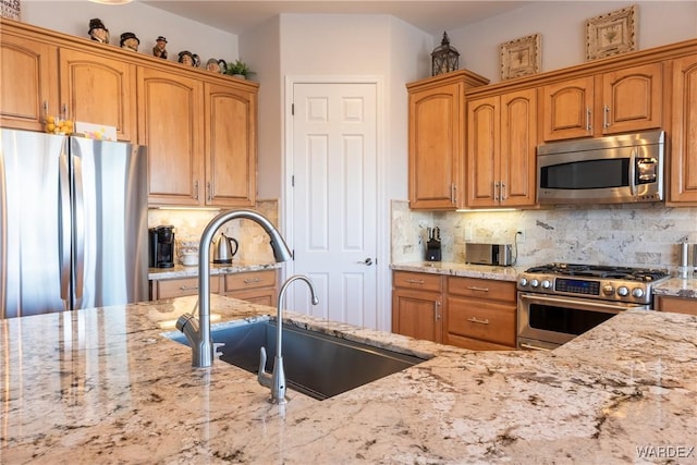 kitchen with appliances with stainless steel finishes, a sink, light stone counters, and decorative backsplash