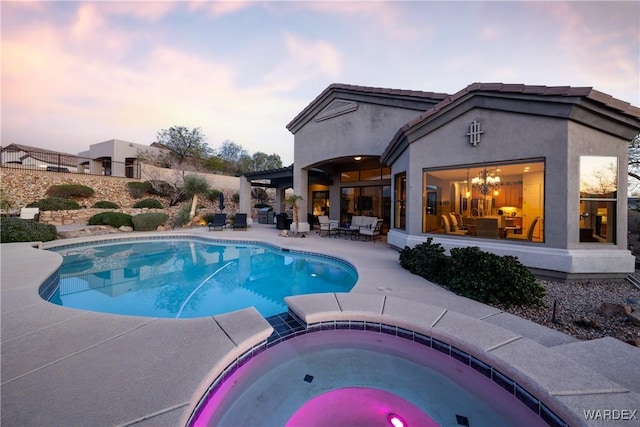 pool at dusk featuring a patio, fence, and a pool with connected hot tub