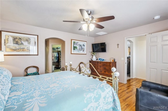 bedroom featuring a spacious closet, light wood-style flooring, arched walkways, and ceiling fan