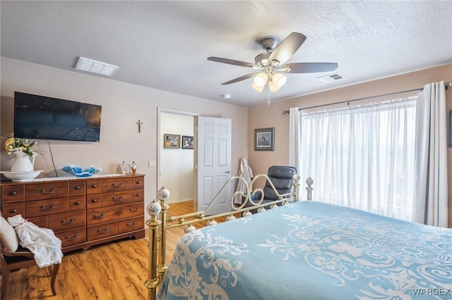 bedroom featuring light wood-style floors, visible vents, a ceiling fan, and a textured ceiling