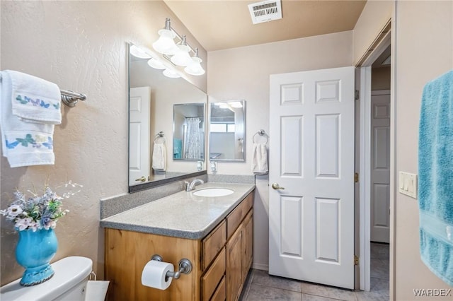 bathroom with tile patterned floors, a textured wall, visible vents, toilet, and vanity
