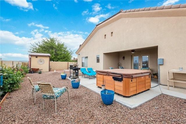 back of house featuring a fenced backyard, stucco siding, a patio area, a storage unit, and a hot tub