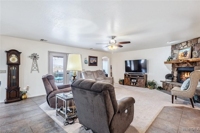 living area with tile patterned floors, a stone fireplace, visible vents, a ceiling fan, and arched walkways