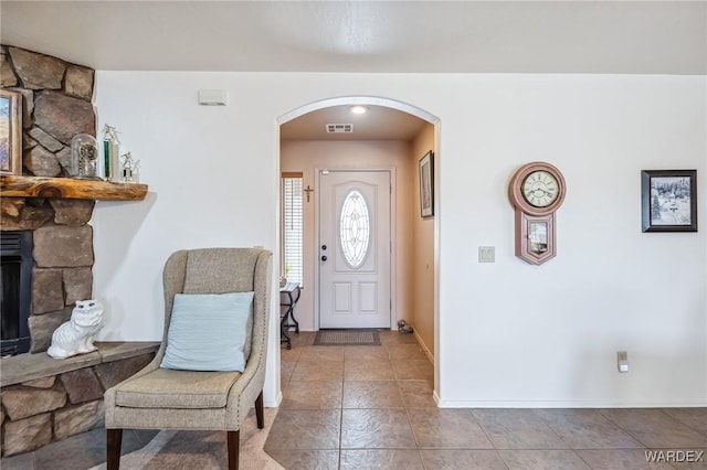 foyer entrance featuring arched walkways, baseboards, visible vents, tile patterned flooring, and a fireplace